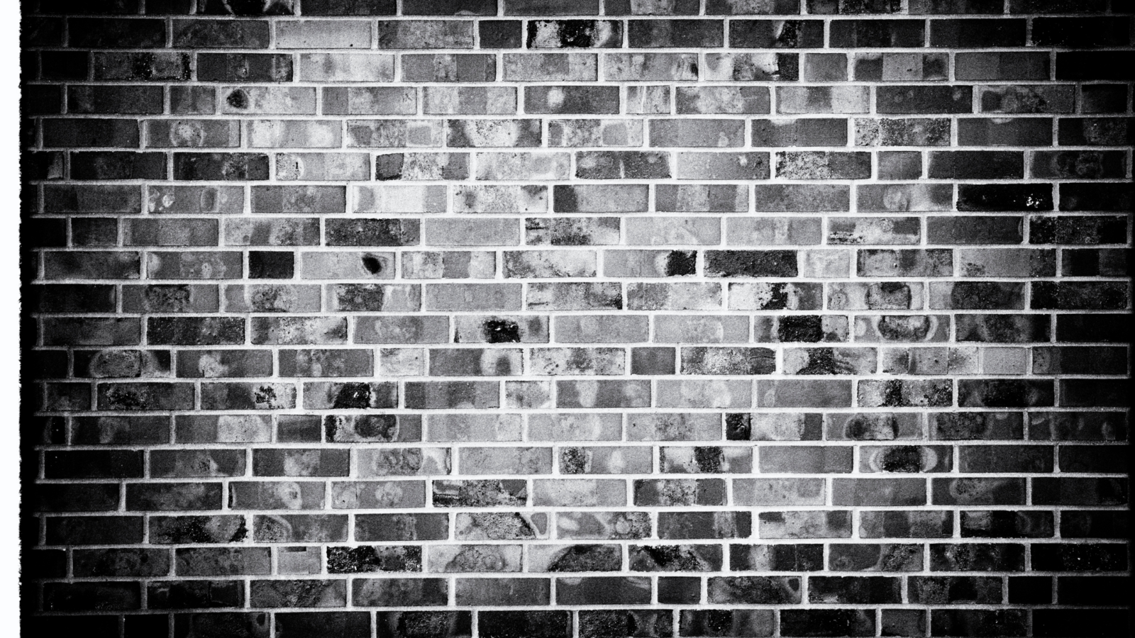 Black and white image of a brick wall with a consistent rectangular brick pattern and varied textures.
