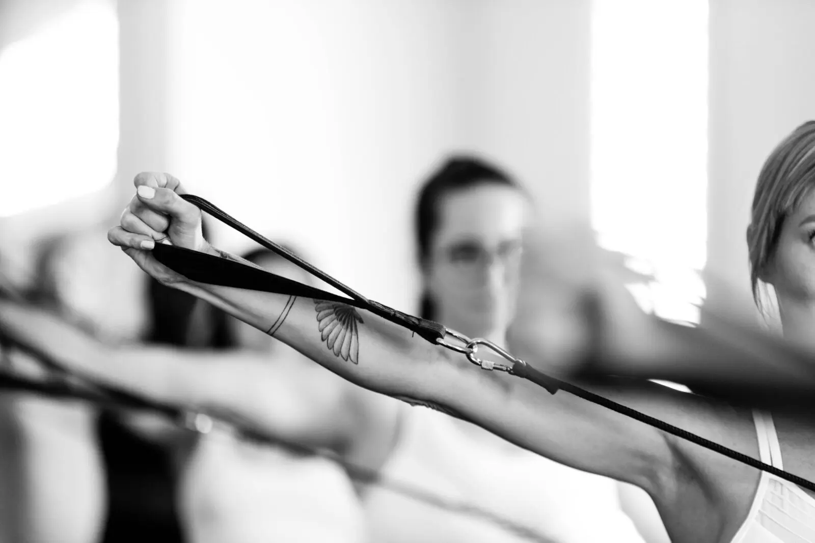 Close-up of a tattooed arm pulling a resistance band during a group exercise session in black and white
