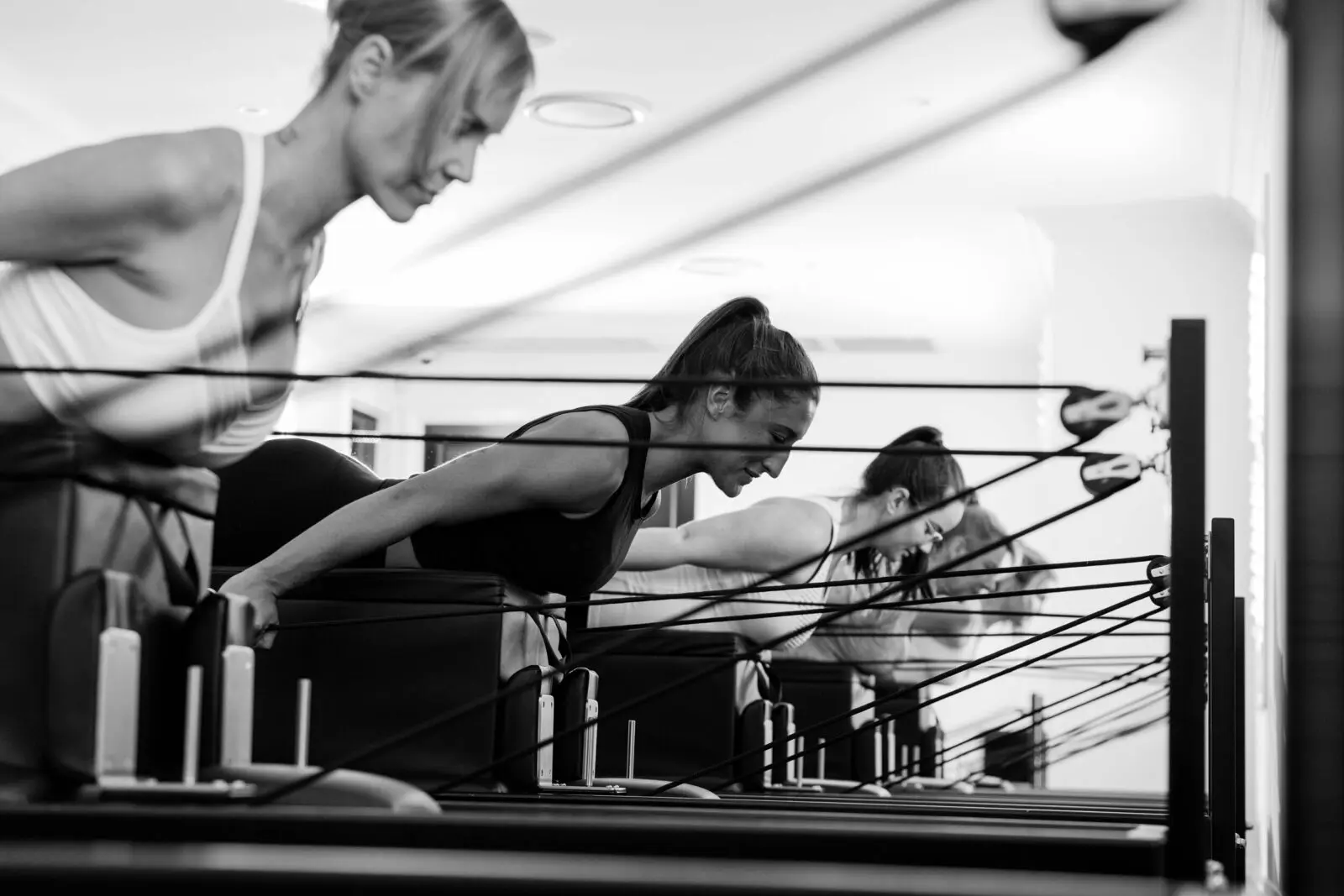 Women exercising on Pilates reformer machines performing stretching exercises with resistance cords.