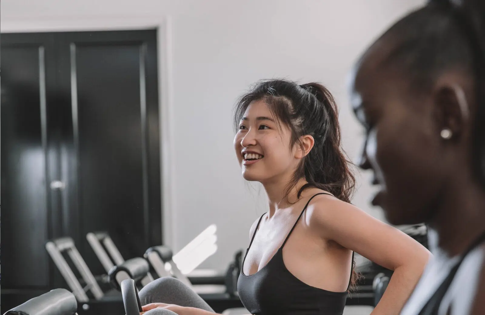 Two women sitting and talking in a gym with exercise equipment in the background