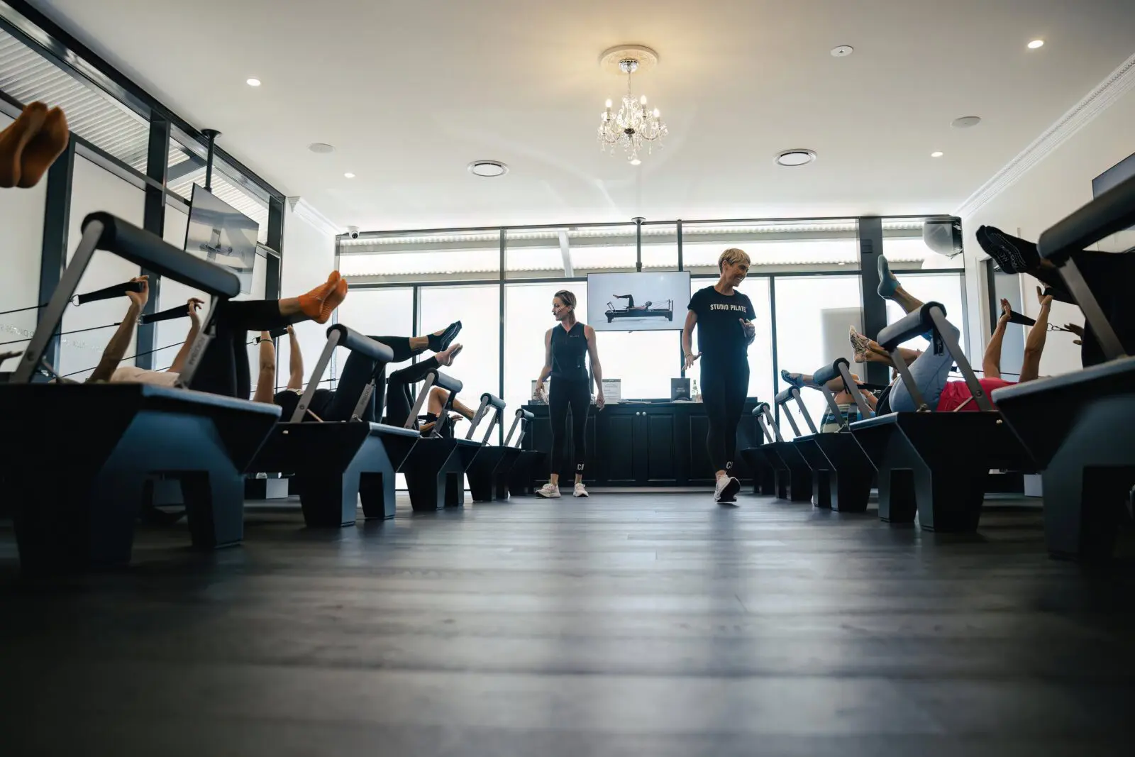 Pilates studio with people exercising on reformers and two instructors overseeing the session.
