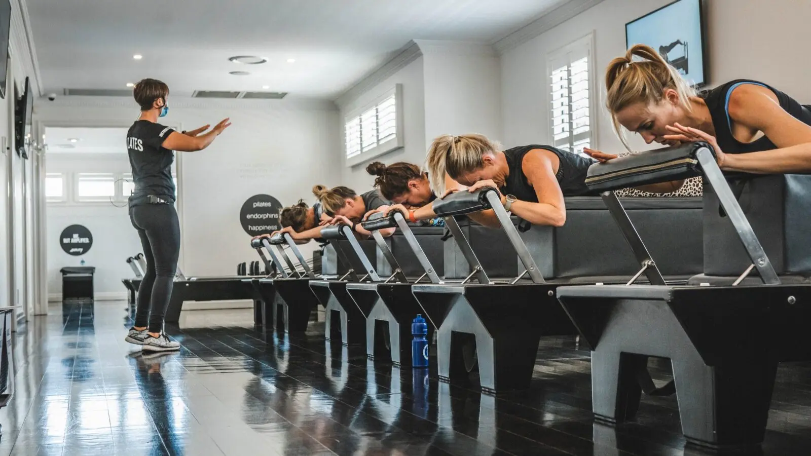 Women exercising on Pilates reformer machines with instructor giving directions in studio.