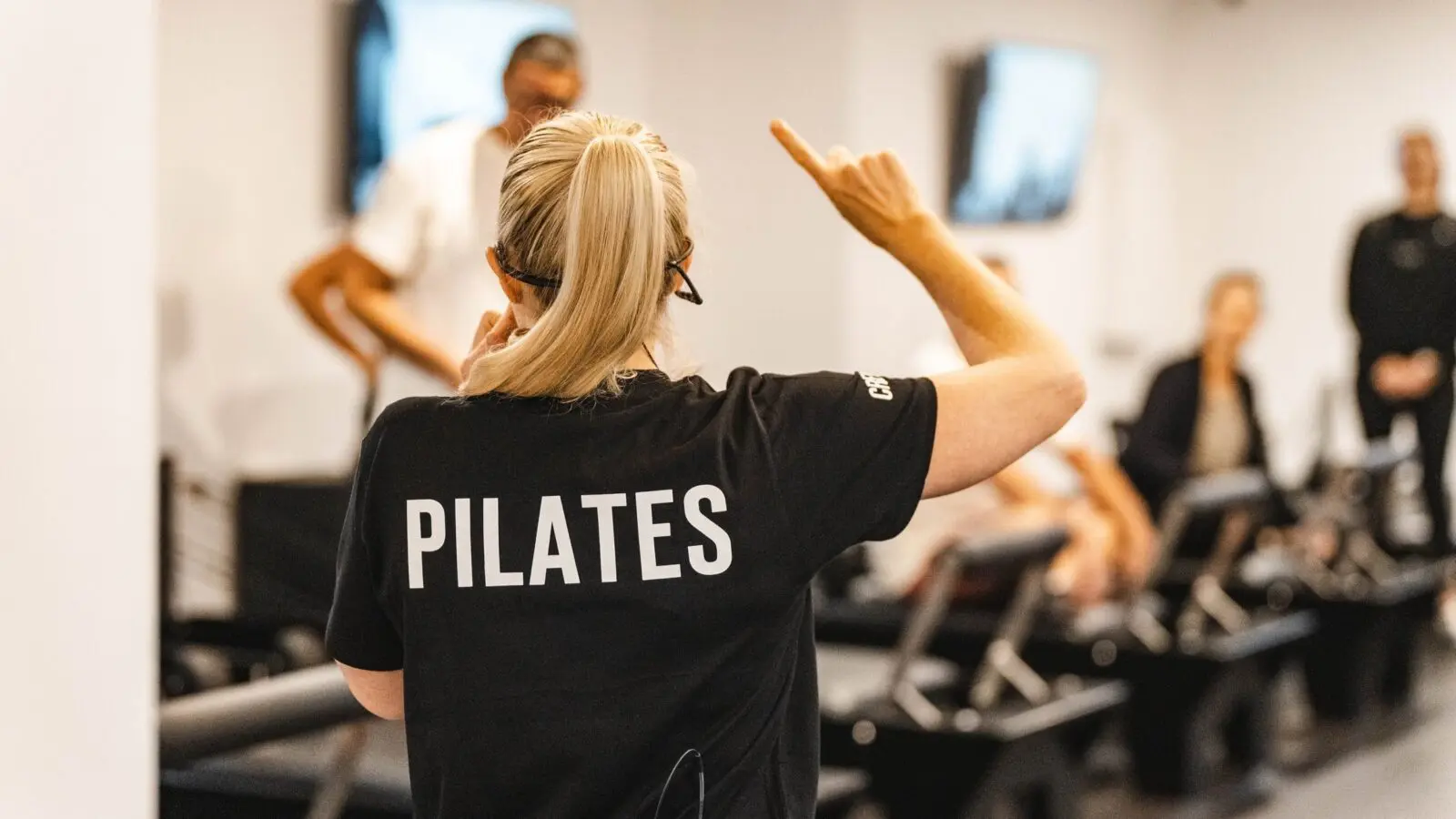 Pilates instructor leading a class with participants on reformer machines in a studio.