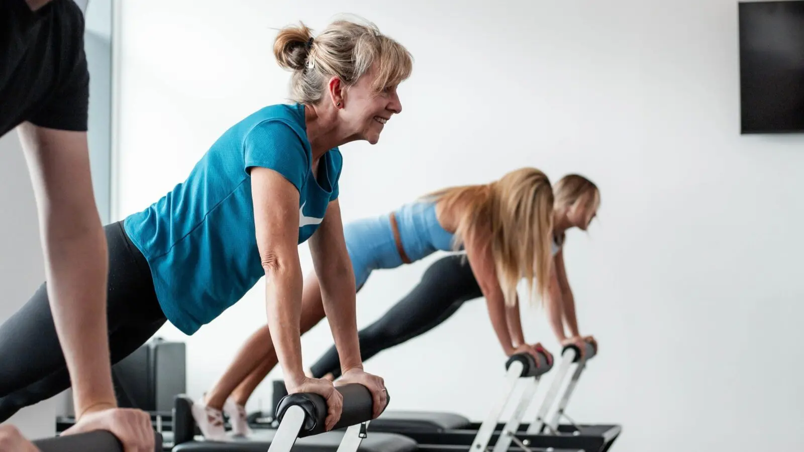People exercising indoors performing plank exercises on reformer machines in a fitness studio.