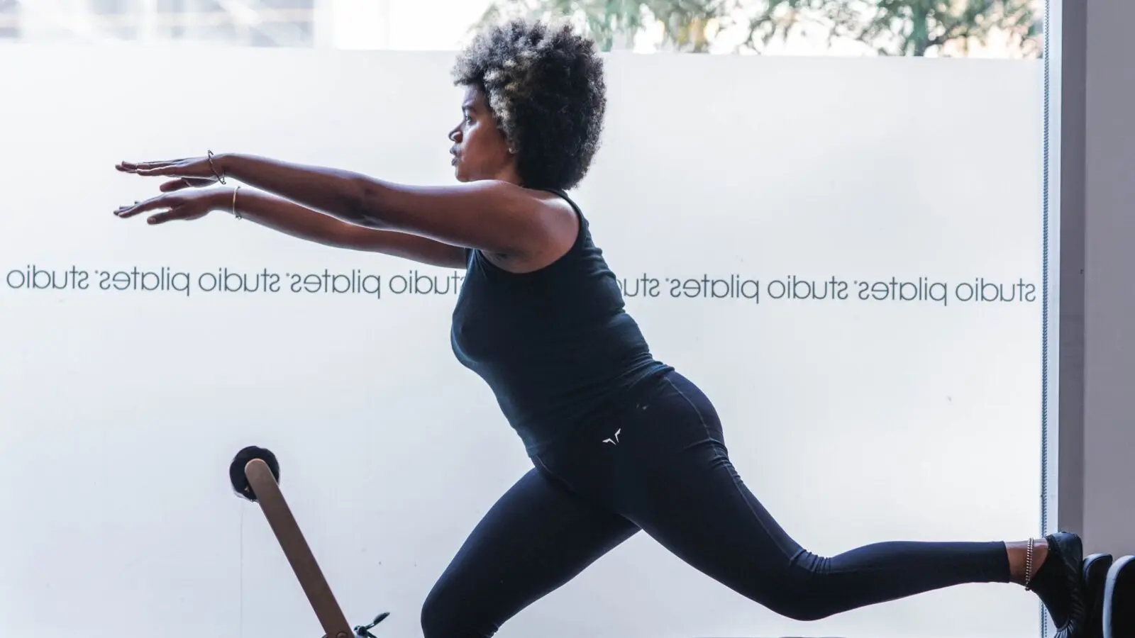 Person performing a balance exercise with arms extended on a Pilates reformer machine.