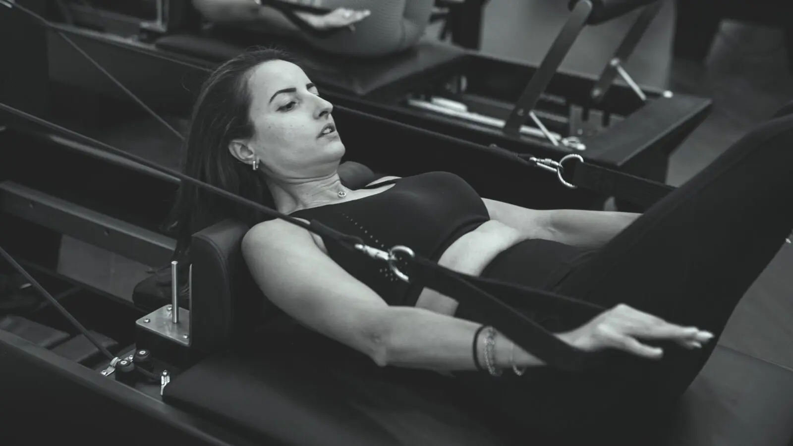Woman exercising on a Pilates reformer machine using resistance cables in a gym setting