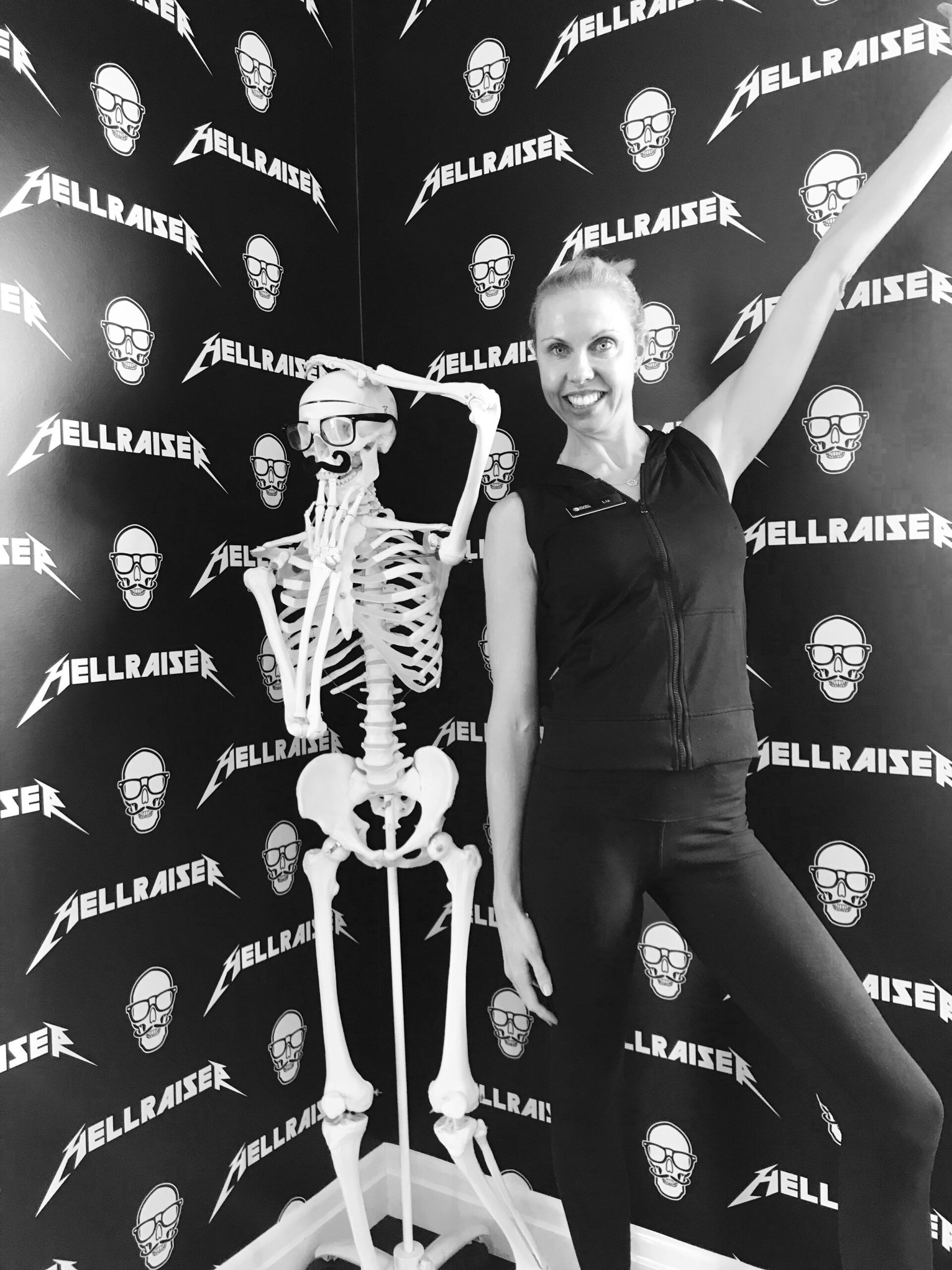 Woman posing with a skeleton model wearing glasses and a mustache in front of Hellraiser backdrop.