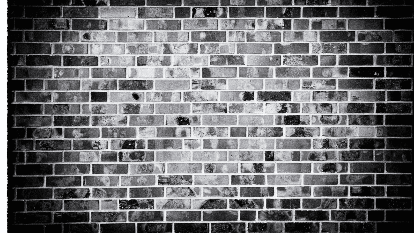Black and white image of a brick wall with a consistent rectangular brick pattern and varied textures.