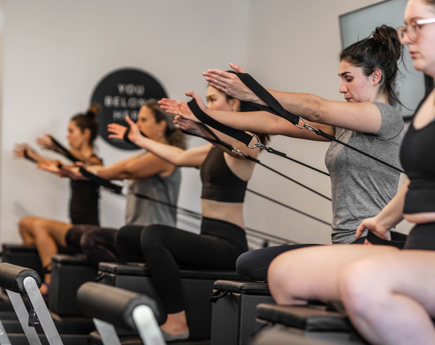 Women seated on Pilates reformer machines performing resistance band exercises in a fitness studio