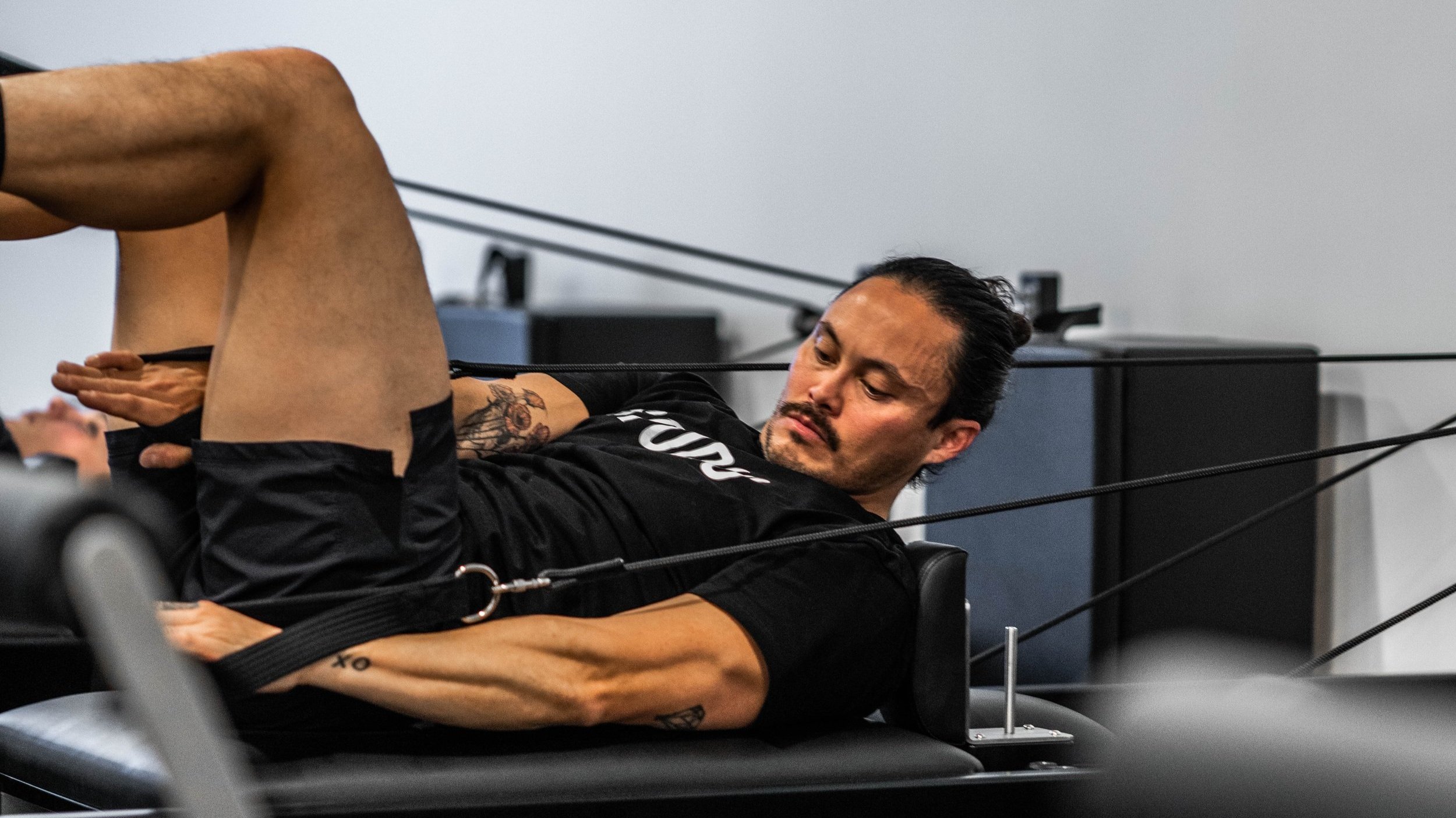 Man lying on Pilates reformer machine exercising with resistance bands in gym setting