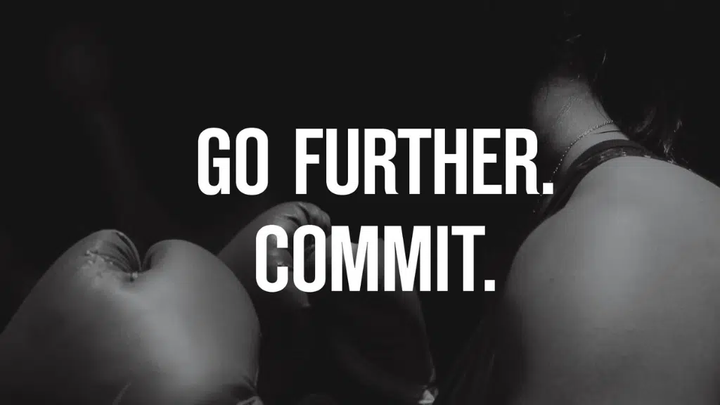 Boxing gloves close-up with person and motivational text go further commit in bold letters.
