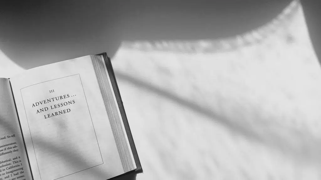 Open book with a page titled Adventures and Lessons Learned under sunlight shadows.