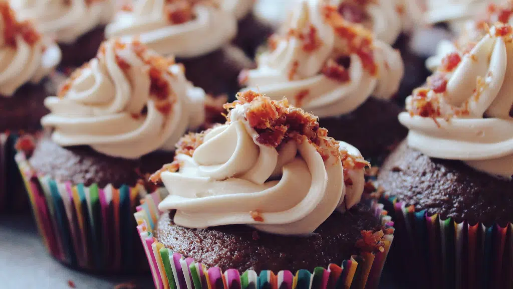 Chocolate cupcakes with white swirled frosting and crumbled topping in colorful liners.