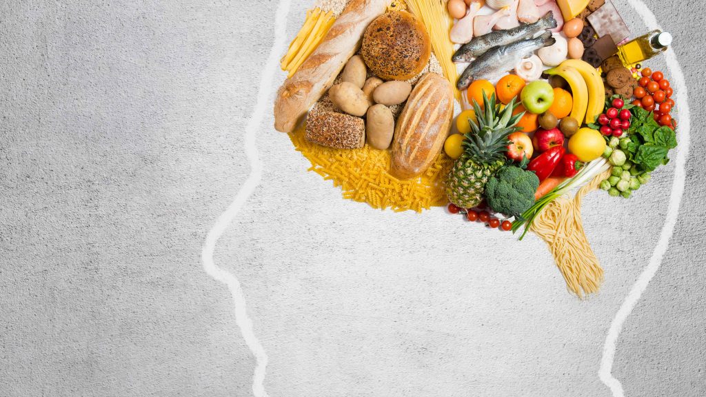 Silhouette of a human head filled with various foods like bread, fruits, vegetables, fish, eggs, and oil.