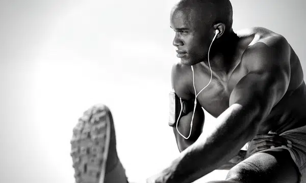 Muscular man wearing earphones stretching leg while seated, preparing for workout session.